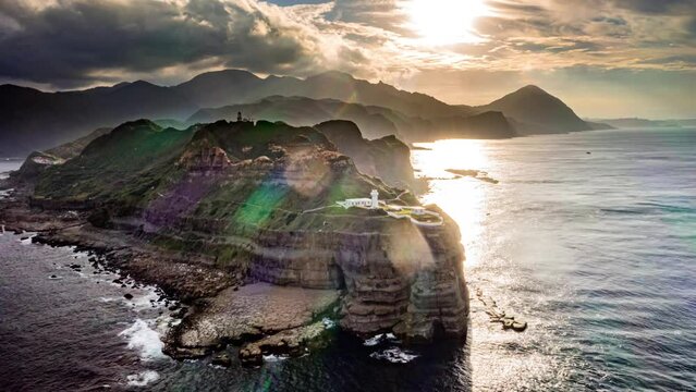 Drone Hyperlapse, Time-lapse, aerial view A Bitoujiao lighthouse with a white dome on the nose stands on the tip of a cliff in a beautiful landscape coastline and sunset behind, Taiwan, Asia.