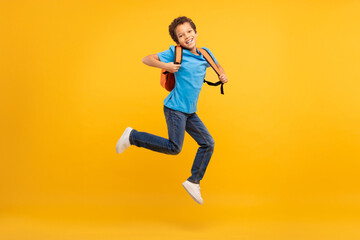 Fototapeta na wymiar Energetic boy with backpack jumping, bright yellow background