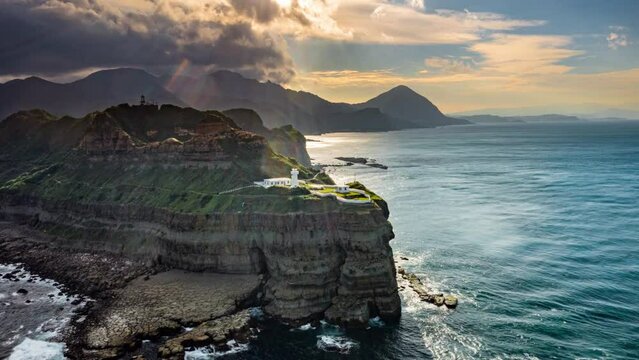 Drone Hyperlapse, Time-lapse, aerial view A Bitoujiao lighthouse with a white dome on the nose stands on the tip of a cliff in a beautiful landscape coastline and sunset behind, Taiwan, Asia.