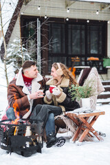 Young loving couple spending winter holidays in a countryside cottage house. Wearing warm clothes, knitted sweaters, mittens. Hot drinks. Cozy Christmas atmosphere, New Year's Eve, snowy frosty day