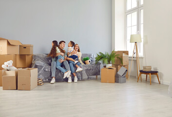 Happy in our new family home. Funny young Caucasian family is happy, having fun, laughing and hugging in house they just moved into. Family on sofa among cardboard boxes. Family relocation concept.