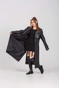 model girl in a black short dress in leather raincoat with glasses in studio with hard spotlight light posing relaxed in studio