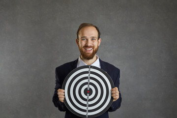 Portrait of happy young man holding shooting target and smiling standing on gray studio background...