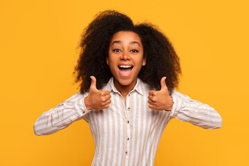 Cheerful black woman giving two thumbs up against yellow wall