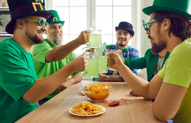 Happy close friends toasting with mugs of green beer at home. Group of cheerful bearded men wearing green carnival headgears drinking beer having fun together. Friendship, home party concept
