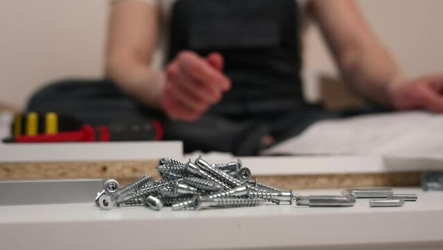 The furniture assembler looks at the instruction, takes euro screws in his hand, close-up. Self-assembly of furniture. The concept of moving, repairing, assembling furniture