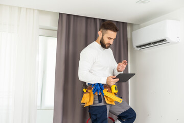 Young Technician using digital tablet and pen checking air conditioner in house room. Air Conditioning system installation and repairing concept