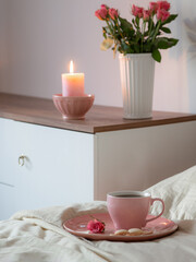 pink cup of coffee on bed with flowers in vase  in white bedroom