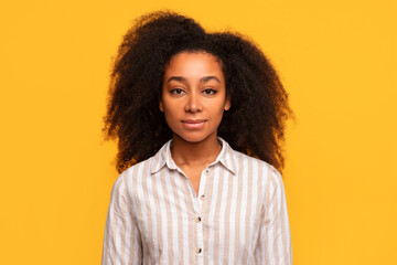 Serene black woman with curly hair in striped shirt on yellow background