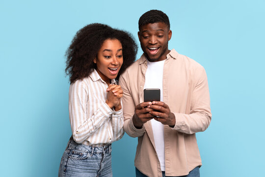 Excited black couple viewing smartphone together on blue background - Powered by Adobe