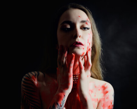 Portrait of young woman with red paint on her chest on dark background.