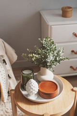 cozy spring home details. House plant, candle and decorations composition on coffee table with chair on background.