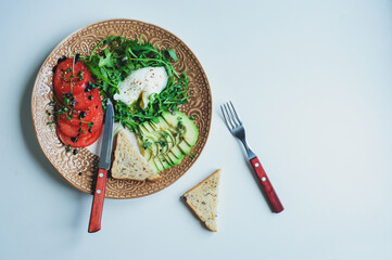 healthy diet vegetarian breakfast - poached egg, whole grain bread, tomatoes, avocado, arugula salad with olive oil and micro green