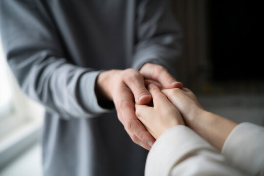 Two people engage in a compassionate touch, offering emotional support through a simple but powerful gesture of connected hands.