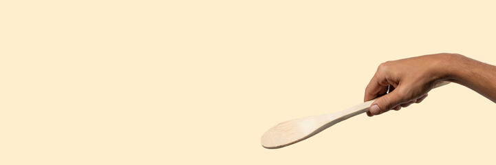 Male hand holding wooden spoon on light beige background.