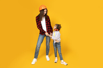 Mother and daughter in accessories for construction, on a yellow background. - obrazy, fototapety, plakaty