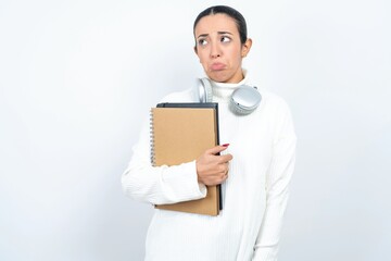 Dissatisfied Young beautiful woman wearing white turtleneck sweater purses lips and has unhappy...
