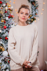 Portrait of an attractive, young woman posing against the background of a Christmas tree and New Year decorations.