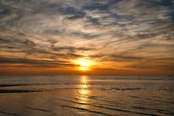 Sunset, illuminated sea. Sandy beach in the foreground. Light waves. Baltic Sea