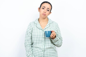 Beautiful young woman wearing green plaid pyjama and holding a cup depressed and worry for...