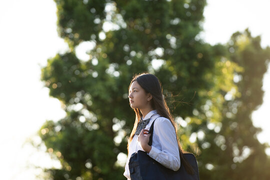 制服姿で大きな木をバックに遠くを見ている女子学生