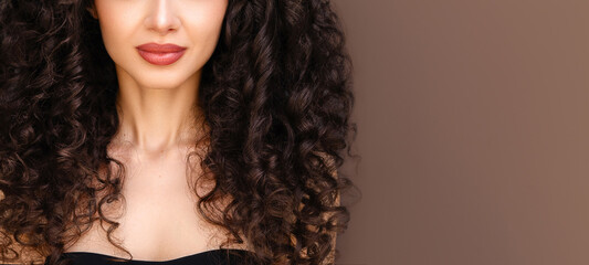 Curly hair care. Beauty portrait of young beautiful brunette female model with wavy healthy dense curls against brown background. - obrazy, fototapety, plakaty