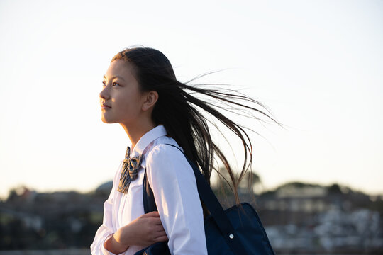 西陽に照らされ髪をなびかせている制服姿の女子学生