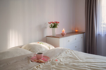 pink cup of coffee on bed with flowers in vase  in white bedroom