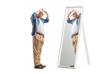 Full length profile shot of a mature man combing hair in front of a mirror