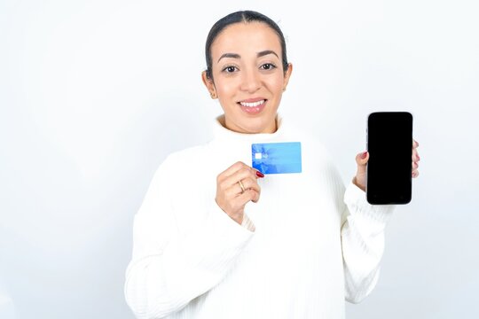 Photo of adorable Young beautiful woman wearing white turtleneck sweater holding credit card and Smartphone. Reserved for online purchases