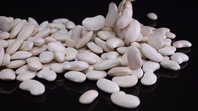 White beans gently descending onto a reflective black surface from two glass containers, highlighting a key ingredient in vegan cuisine.