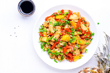 Stir fryed chicken slices with fresh pineapple, paprika, chives, soy sauce and sesame seeds. Asian cuisine dish. White table background, top view