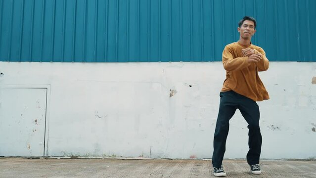Hispanic man stretch arms and dance street dancing in front of wall. Motion shot of dancer or choreographer in casual outfit practicing b-boy dancing in hip hop style. Outdoor sport 2024. hiphop.