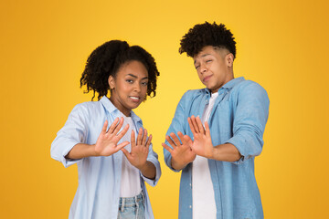 A cheerful young woman and man stand back to back against a vibrant yellow background