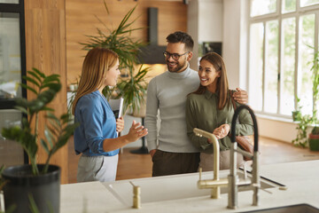 Female shop assistant helping young couple choose new kitchen faucet