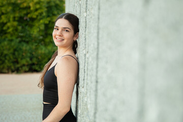 chica deportista sonriente apoyada en un muro en un parque tras hacer deporte al aire libre. Vida saludable. mujer joven.