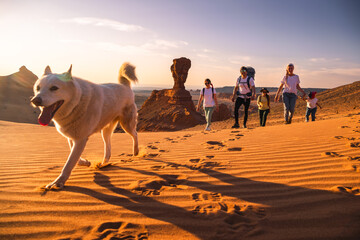 Big family father, mother and little daughters walks with white dog in Gobi desert - obrazy, fototapety, plakaty