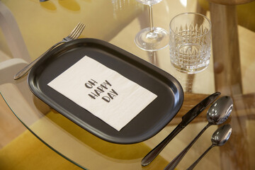 Dining table arrangement with ceramic black rectangular dinner plates, silver flatware set and glasses for water and wine.	