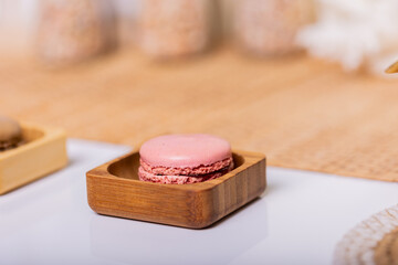 Delicate pink macaron cookie in a wooden bowl on a white table surrounded by boho-style decor. Perfect for bakery banners.
