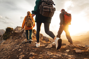 Three young hikers with small backpacks walks in sunset mountains. Close up photo of tourist legs in sunset light