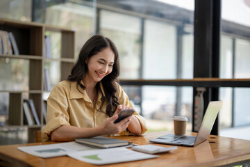 Attractive Asian businesswoman sitting using mobile phone at table in office