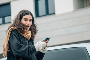 teenager girl with surprise gesture and mobile phone on the street in autumn