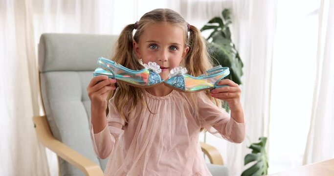 Beautiful cute girl with ponytails examines elegant iridescent blue shoes in her hands. Cute little fashionista. Happy child girl try on outfits