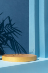 A round golden podium on an abstract blue background with a shadow of palm leaves. A scene with a geometric background. Backdrop for the product presentation.