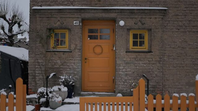 Beautiful entrance to scandinavian style house with wooden yellow door and christmas wreath. Homemade diy xmas decoration. Winter city doors and landscape. Winter ornaments and nordic lifestyle