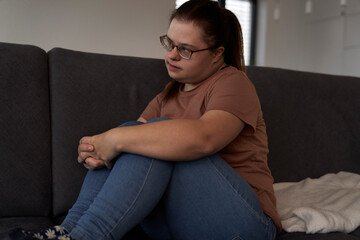 Thoughtful down syndrome woman sitting on sofa and looking away