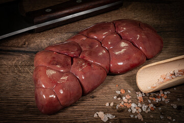 Raw Beef kidney, fresh sliced offal meat on plate. Dark background. Top view