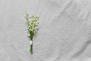 Bouquet of white lily of the valley flowers on a light gray linen background. Women's or Mother's Day concept with white flowers on a plain background. Empty card for congratulations, copy space.