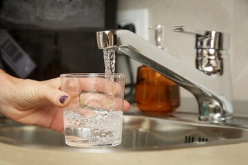 Filling up a glass with fresh drinking water from kitchen faucet - obrazy, fototapety, plakaty
