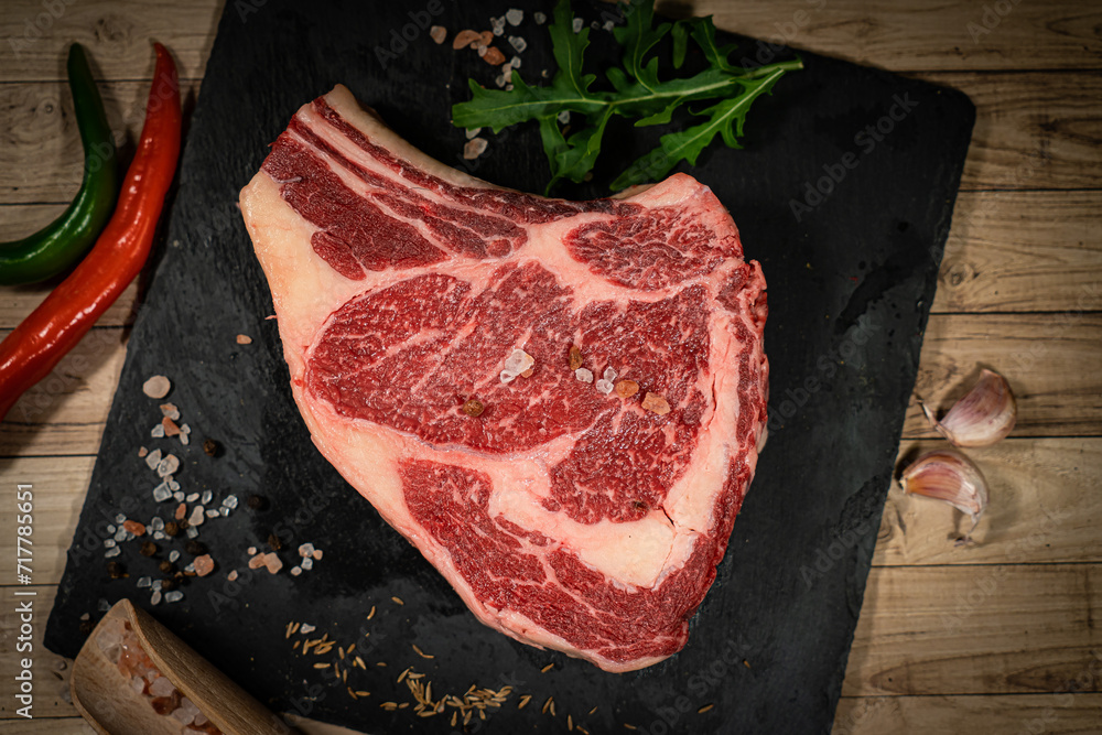 Wall mural raw cowboy steak with seasonings on wooden background, prime rib eye on bone, top view